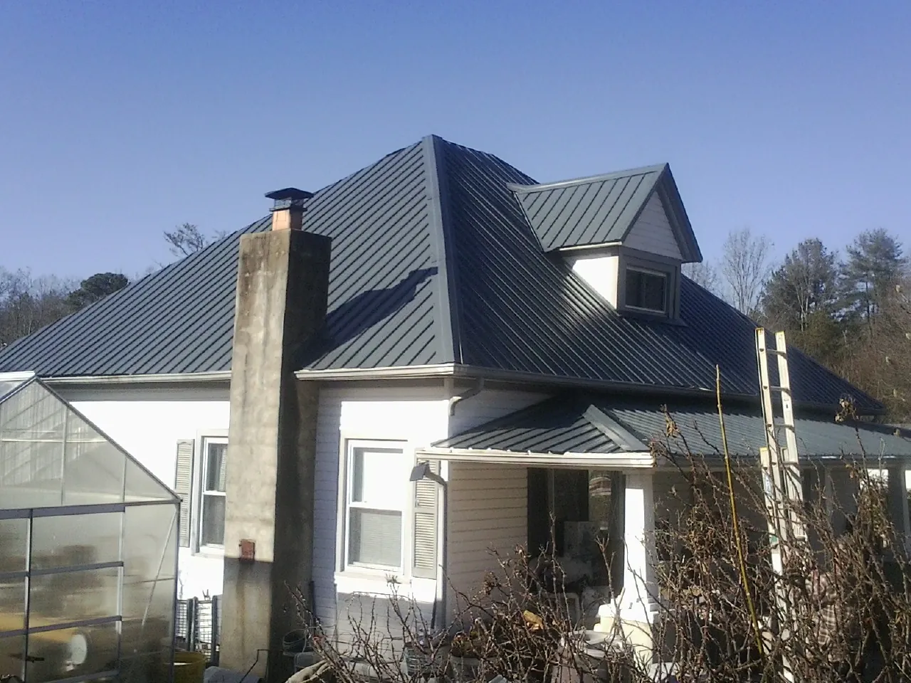 Dark blue standing seam metal roof on a white farmhouse with dormer — Slate & Tile Roof Repair by Roofing Brothers in Barton