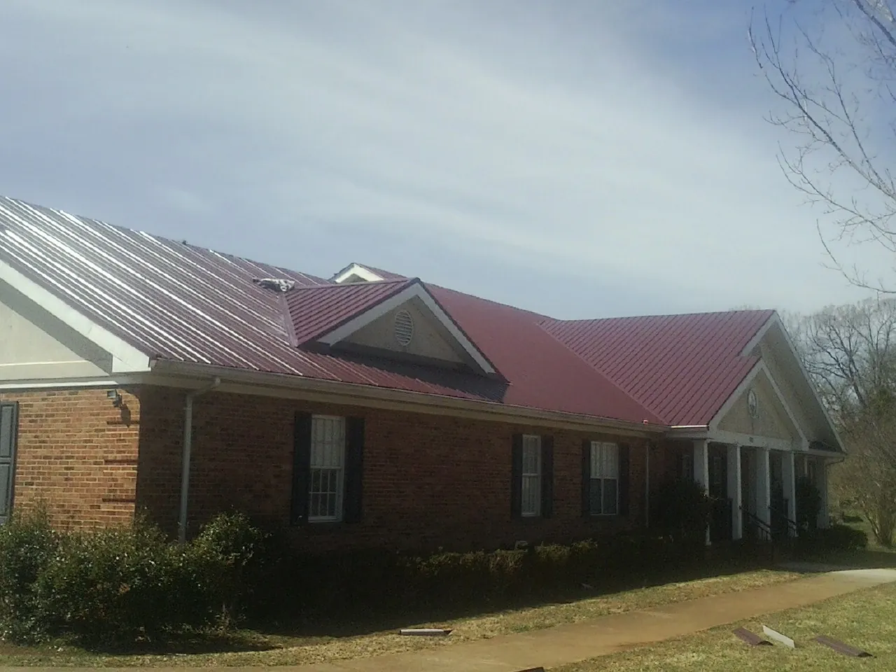 Red metal roof with gabled entries on a long brick building, from a Hail Damage Roof Repair job in Barton