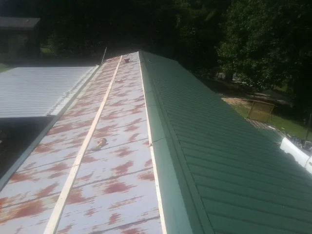 Old rusted panels beside newly installed green metal roofing — Wind Damage Roof Repair by Roofing Brothers in Barton